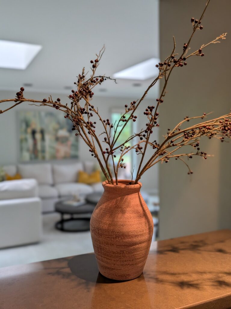 This staging photo shows a rustic vase with long faux stems with red berries artfully arranged on a counter between the kitchen and the living room.